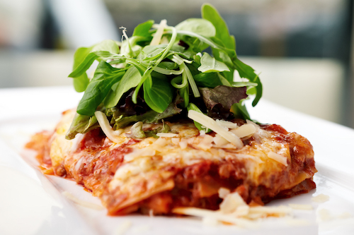 Lasagna served on a white plate with salad