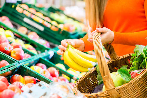 Woman in supermarket at the fruit shelf shopping for groceries, she is putting a banana in her basket