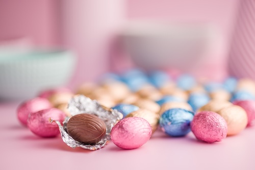 Chocolate easter eggs wrapped in multi colored foil on a pink background.